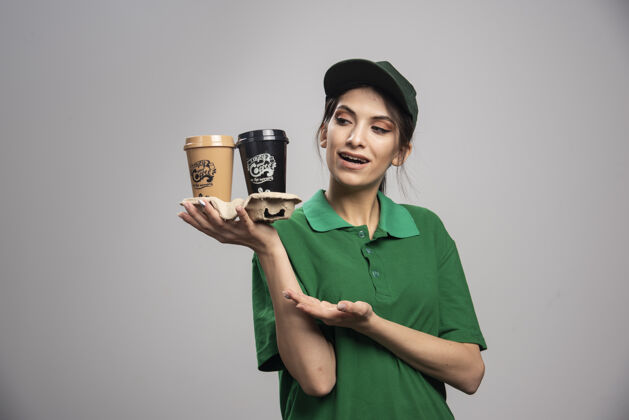 工作穿着绿色制服的女送货员端着咖啡站着工人送货咖啡