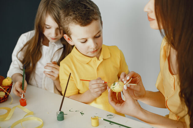 黄色孩子们画鸡蛋妈妈教孩子们坐在一张白色的桌子旁家庭小童年