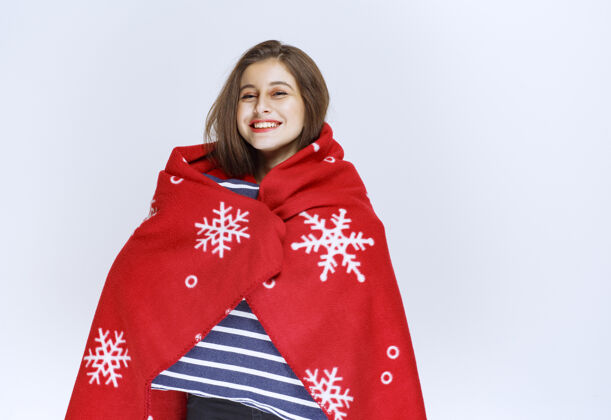 女人一个年轻的女人用一条红色的暖和的毯子盖着自己 手里拿着一条蓝色的条纹毯子冬天失眠夜晚
