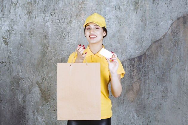 运输穿着黄色制服的女快递员送了一个纸板购物袋 并出示了她的名片女性员工订单