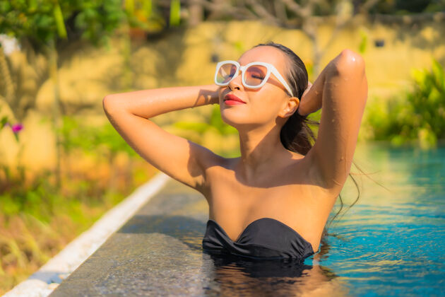 阳光美丽的亚洲年轻女子在游泳池里放松的画像帽子年轻人奢华
