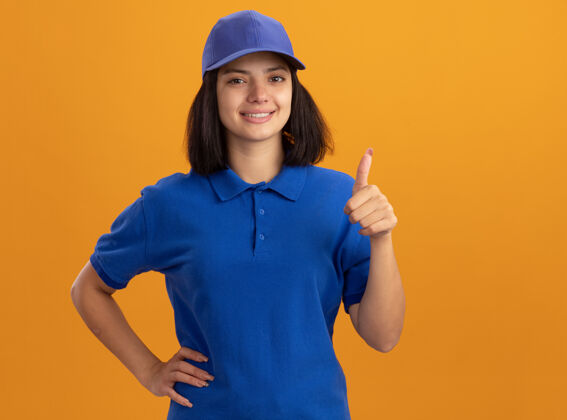 年轻身穿蓝色制服 头戴鸭舌帽 站在橙色墙壁上微笑着露出肚子的年轻送货女孩制服帽子站着