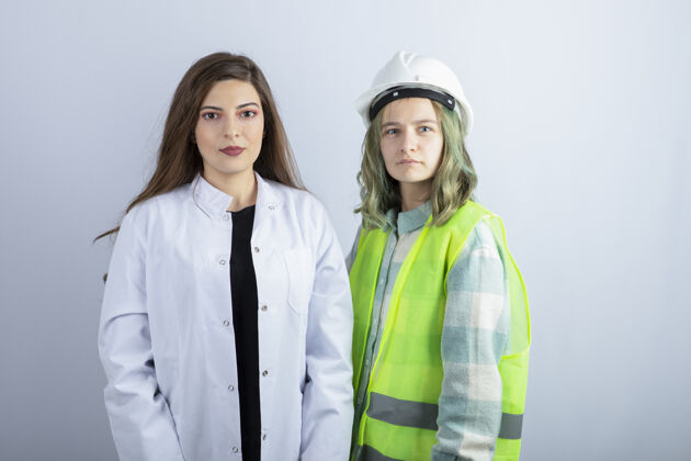 年轻人年轻的女医生和女工程师站在白色的墙上高质量的照片头盔职业漂亮