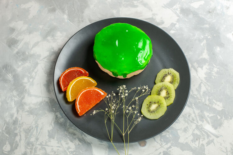生的俯瞰美味的小蛋糕与绿色糖衣内板上的白色表面蛋糕双份甜甜的糖派小盘子珠宝