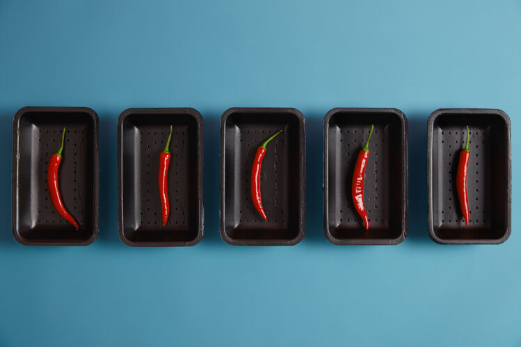 顶部你的菜要有辛辣的配料在蓝色背景上隔离的黑色托盘上放一层薄薄的红辣椒 在超市里包装 可以生吃也可以干吃 用来做辣椒粉 给烤肉调味包装辣椒调味料