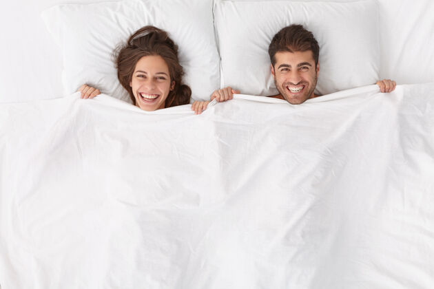 配偶快乐的夫妻享受在一起的时光 躺在白毯子下 有积极的表情和微笑 呆在床上 睡后醒来或清晨小睡 在深度健康的夜晚后感觉焕然一新 睡眠高兴头顶