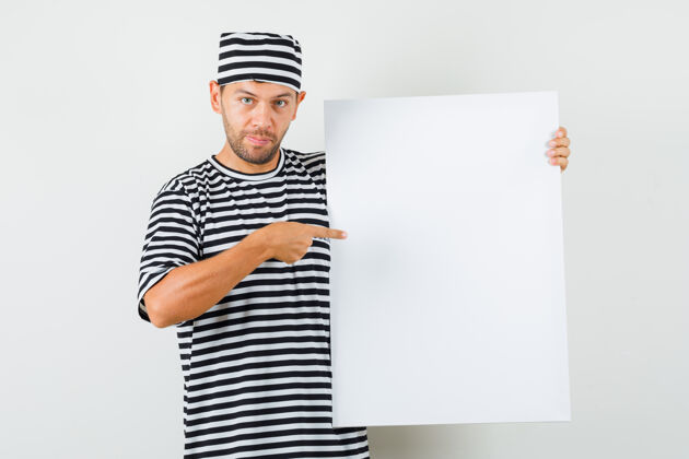 衬衫一个年轻人指着一块空白的帆布 戴着条纹t恤帽子 看上去很积极帽子自信男士