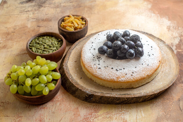 蓝莓侧面特写镜头蛋糕一块蛋糕放在板上绿色葡萄葡萄干南瓜籽在碗里蛋糕水果碗