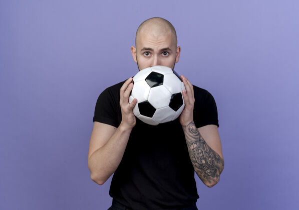 球看着镜头年轻的运动型男子脸上的球孤立在紫色的背景脸封面年轻
