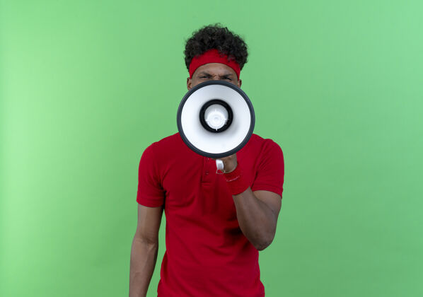 腕带看着镜头 戴着头带和腕带的年轻的美国黑人运动型男子在绿色背景下用扬声器讲话非裔美国人头带运动