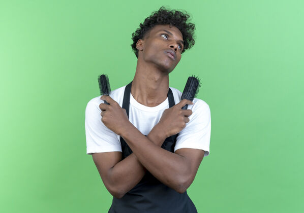 非裔美国人看着身边疲惫的年轻美国黑人男理发师穿着制服 肩上拿着梳子 隔离在绿色的背景上累了理发师年轻