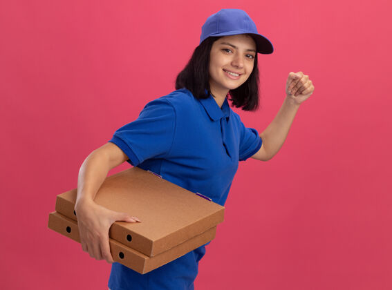 顾客一个穿着蓝色制服 戴着帽子的送货员正在粉红色的墙上为顾客运送披萨盒披萨制服盒子