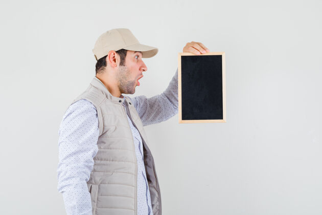 黑板一个穿着米色夹克 戴着帽子的年轻人拿着黑板 惊讶地看着前方自然人时尚
