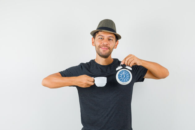 虚拟一个戴着t恤帽子的年轻男人拿着闹钟和一杯饮料 看上去很高兴人类T恤办公室