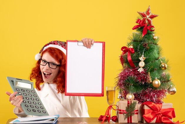 花前视图女医生拿着计算器围着圣诞礼物和圣诞树周围花束颜色