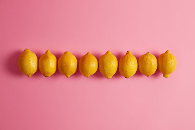 水果黄色的整颗柠檬在粉红色背景下排列成一排柑橘类水果是维生素c和叶酸的良好来源是制造健康水 柠檬水或装饰食品的原料多汁的新鲜的扁平
