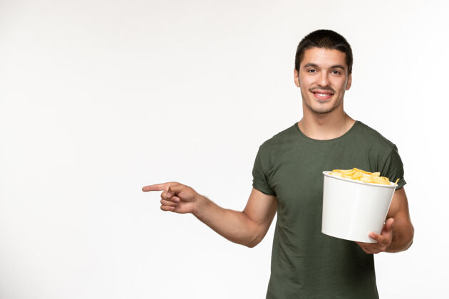 年轻男性正面图身穿绿色t恤的年轻男性 带土豆cips 在白墙上微笑电影人孤独电影电影院电影电影土豆