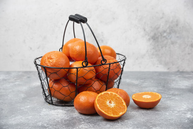 提神石桌上放着一个装满多汁橙子的金属黑色篮子多汁成熟水果