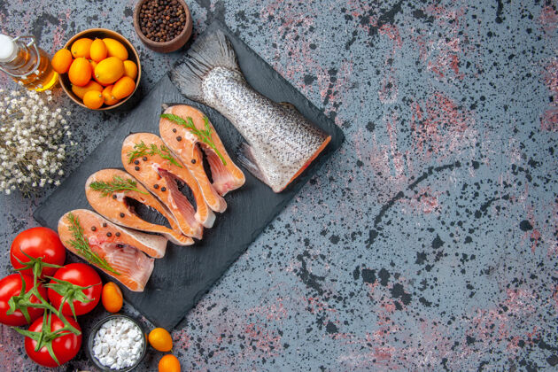 混合物鲜切生鱼的俯视图深色托盘上的绿色调料金橘油瓶上的蓝黑色混色表盘子香料生鱼