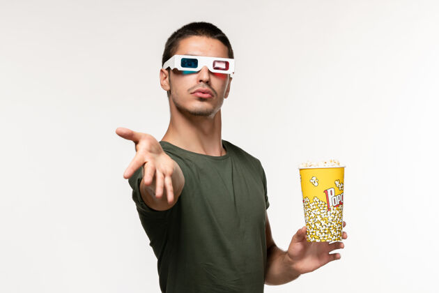 包装正面图身着绿色t恤的年轻男性手持爆米花包戴着d墨镜站在白色墙上孤独的电影院男性电影成人爆米花电影