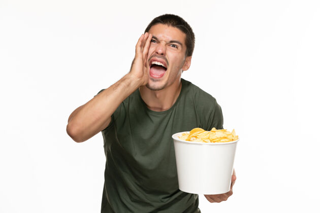土豆正面图身穿绿色t恤的年轻男子拿着一个篮子 里面放着土豆 在白墙上尖叫 孤独地享受着电影观看享受尖叫