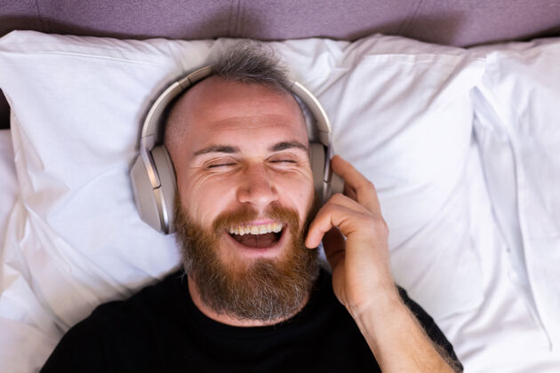 科技快乐的白人男子戴着耳机躺在床上听他最喜欢的音乐 独自休息 跳舞家伙休息无线