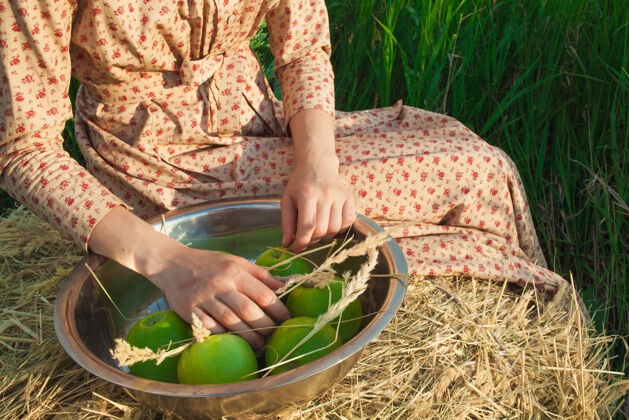 女人坐在草堆上的女人 在绿色的草地上拿着苹果农业年轻乡村