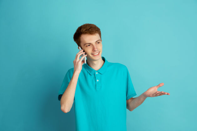 手讲电话 微笑白人年轻人的现代肖像在蓝色工作室 单色男人帅气单色