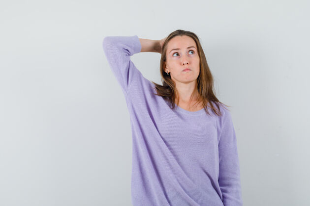 自信年轻的女性手拉在脑后 一边看着淡紫色衬衫 一边沉思着衬衫卷发头发