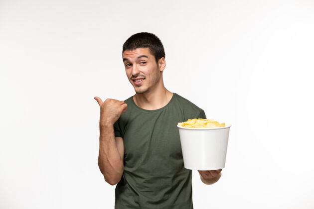成人正面图身着绿色t恤的年轻男性手持土豆cips站在白色墙上孤独的电影人土豆杯子观点
