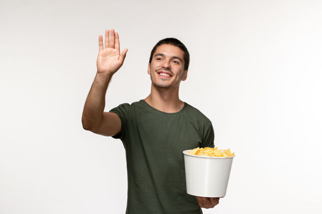 某人正面图：身穿绿色t恤的年轻男性 带土豆cips 在白墙上问候某人电影人男性孤独电影电影院微笑问候土豆
