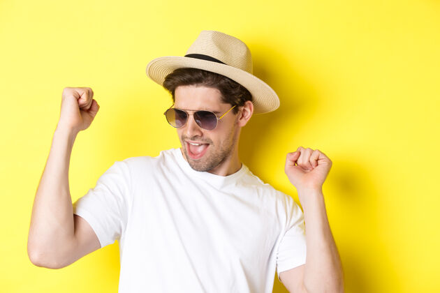帽子旅游和度假的概念旅行中享受假期的男人的特写镜头 跳舞和指指点点 戴着带草帽的太阳镜 黄色背景帅气夏天年轻人