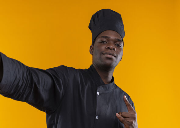 制服年轻自信的非洲裔美国厨师身着厨师制服 假装拿着相机 手势 喇叭 手势 手势 在橙色上留有复印空间信心假装手势