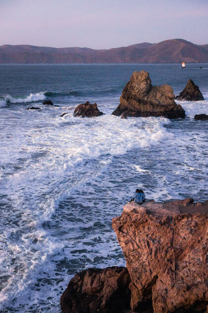 海洋一个穿着黑衬衫的人白天坐在海边的棕色岩石上海角自然人类