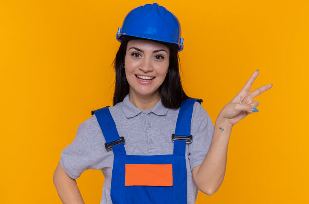 安全穿着施工制服和安全帽的快乐积极的年轻建设者站起来制服女人