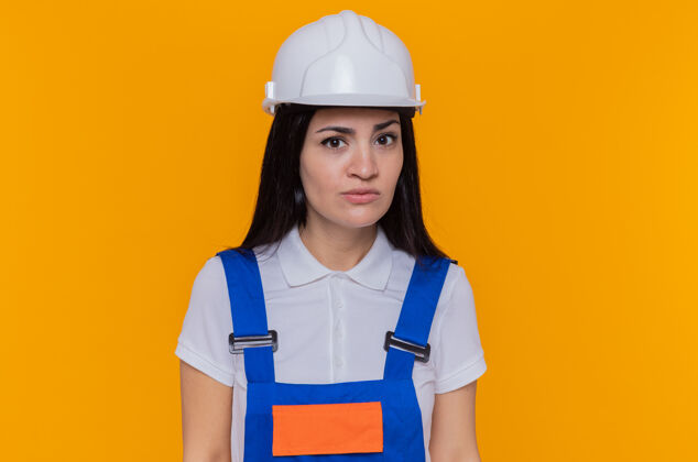 制服年轻的建筑女工穿着建筑制服 戴着安全帽看着摄像机站立建设者女人
