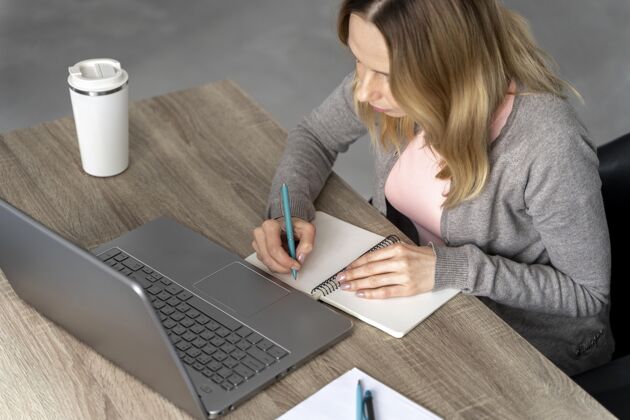 笔记本戴着耳机在笔记本电脑上工作的女人钢笔学习杯子