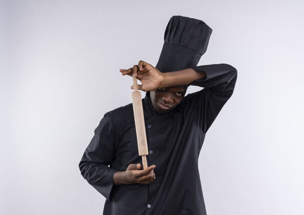 卷年轻恼怒的非洲裔美国厨师穿着厨师制服 拿着擀面杖 看着白色的相机和复印空间年轻空间烹饪