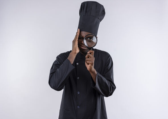 厨师年轻焦急的非洲裔美国厨师身着厨师制服 透过放大镜或放大镜在白色地板上观看 并留有复印空间烹饪玻璃复制
