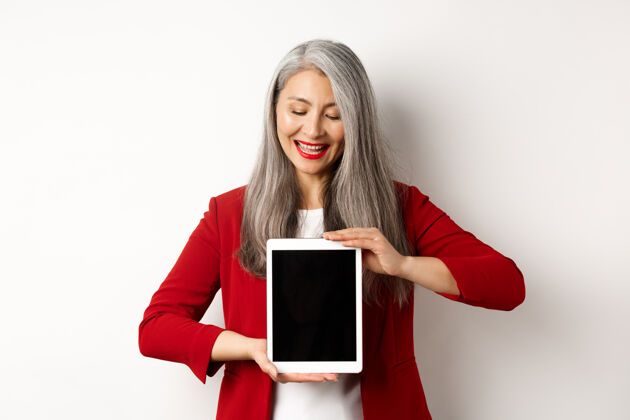 亚洲一位成功的亚洲女商人穿着红色外套 展示着空白的数字平板电脑屏幕 脸上带着喜悦的微笑 白色的背景企业家工作优雅