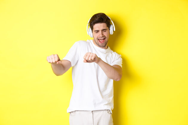 自信很酷的家伙戴着耳机听音乐跳舞 穿着白衣服站在黄色的工作室背景下黄色演播室耳机