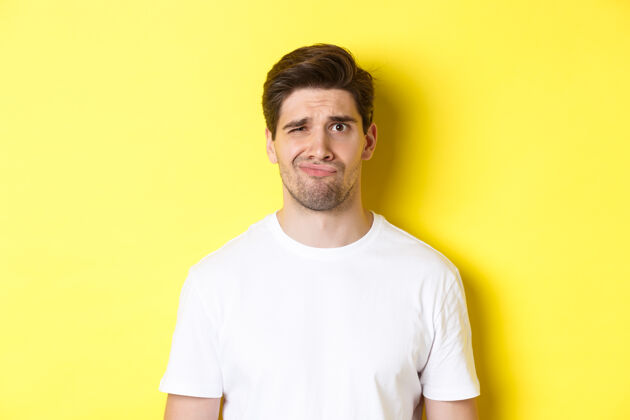 黄色特写镜头里 一个穿着白色t恤的年轻人站在黄色的背景下 神情可疑 表情不满意工作室不高兴男人