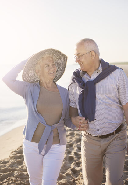 阳光在阳光明媚的日子里散步老年夫妇在沙滩上 退休和暑假的概念约会浪漫日出