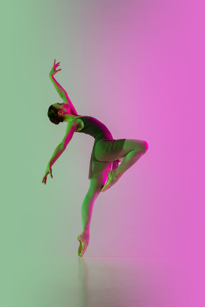 灯光轻年轻而优雅的芭蕾舞演员在霓虹灯下被隔离在渐变的粉绿色墙壁上艺术 动作 动作 灵活性 灵感概念灵活的芭蕾舞演员 失重跳跃情感飞翔健身