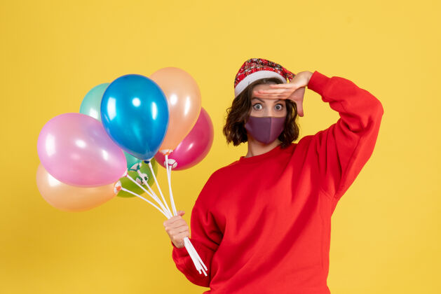 外科面具正面图：戴着面具手持气球的年轻女子在黄色派对上欢庆新年色彩的情感女子气球情感面具
