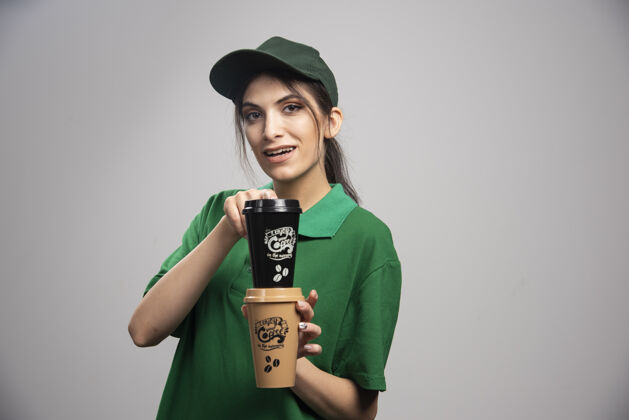 工人穿着绿色制服的送货员拿着咖啡杯摆姿势承运人女孩杯子
