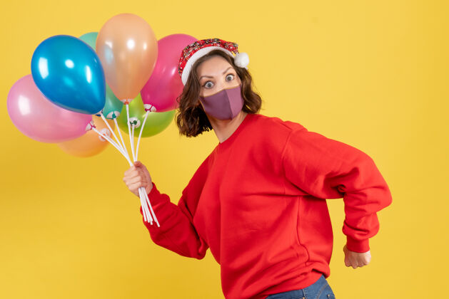 派对正面图：戴着面具手持气球的年轻女子在一个黄色派对上感慨新年色彩庆典的女人庆典面具女人