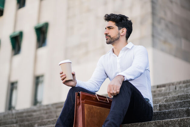 街道一个商人在下班休息时坐在楼梯上喝咖啡的画像商业概念企业家工作男人