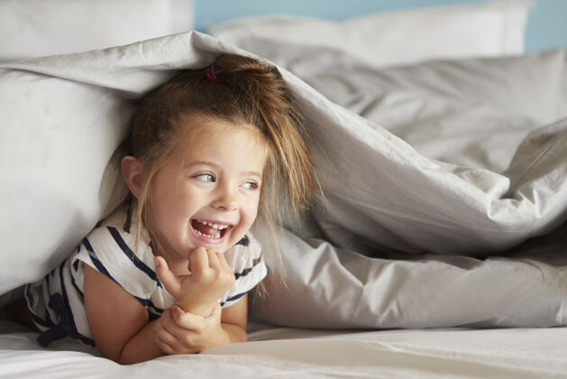 卧室快乐的女孩躲在床单下面躺在前面女孩金发