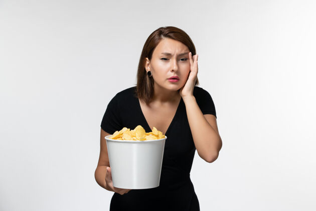 孤独正面图身穿黑色衬衫的年轻女性手持薯片 在白色表面上看电影服务员抱着漂亮